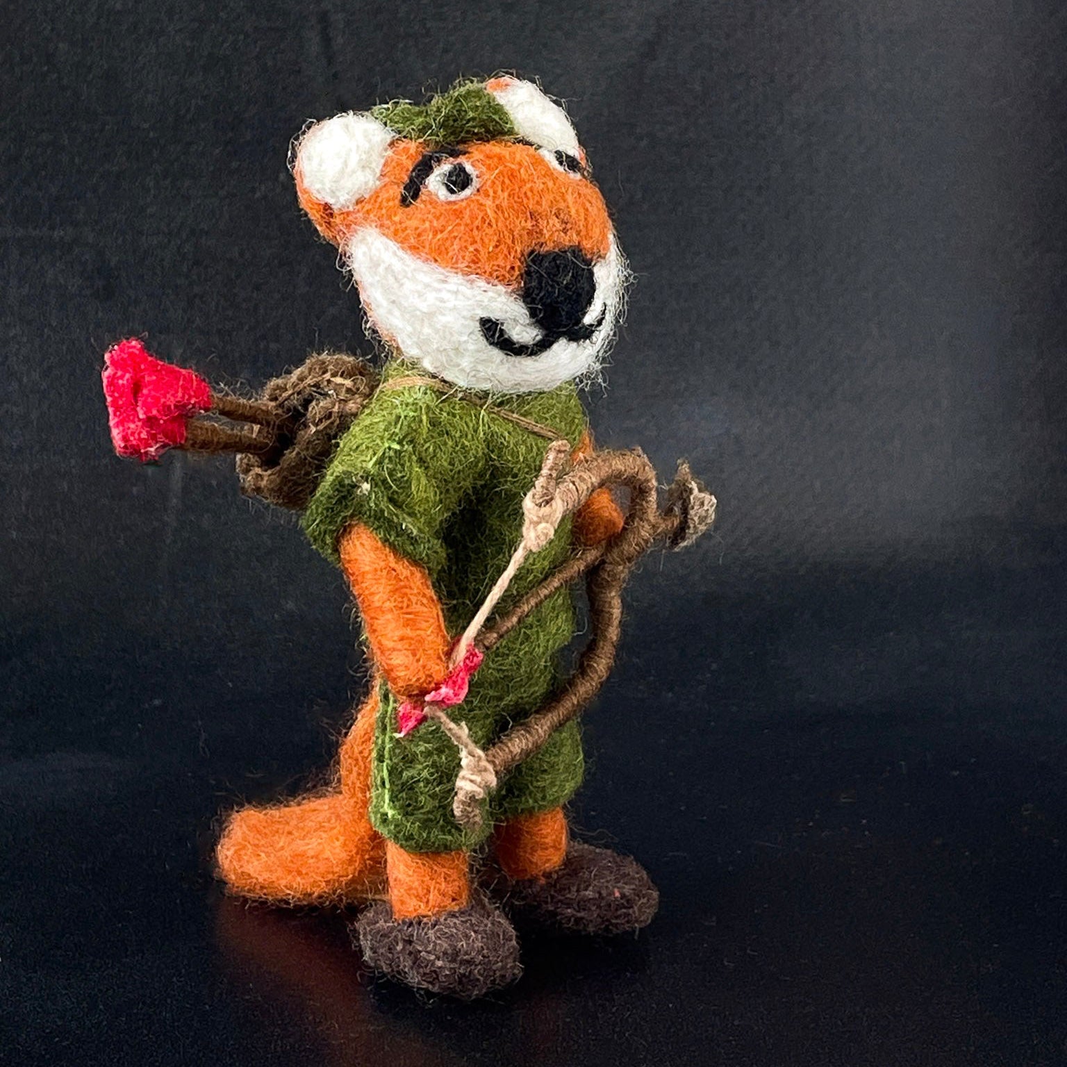 Felted fox figurine holding a bow and arrow on a dark background