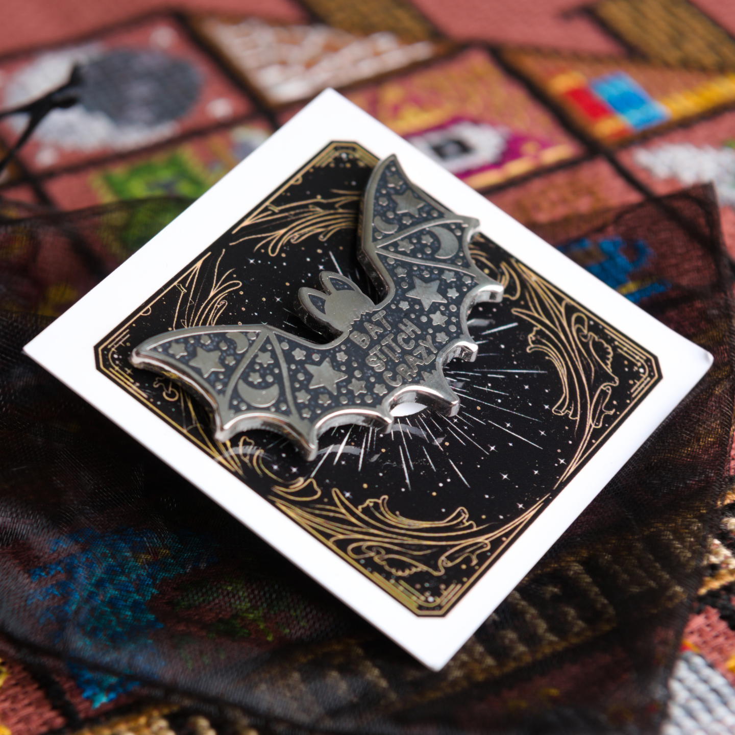Silver and black bat shaped needle minder on a backing card and resting on a black organza gift bag.