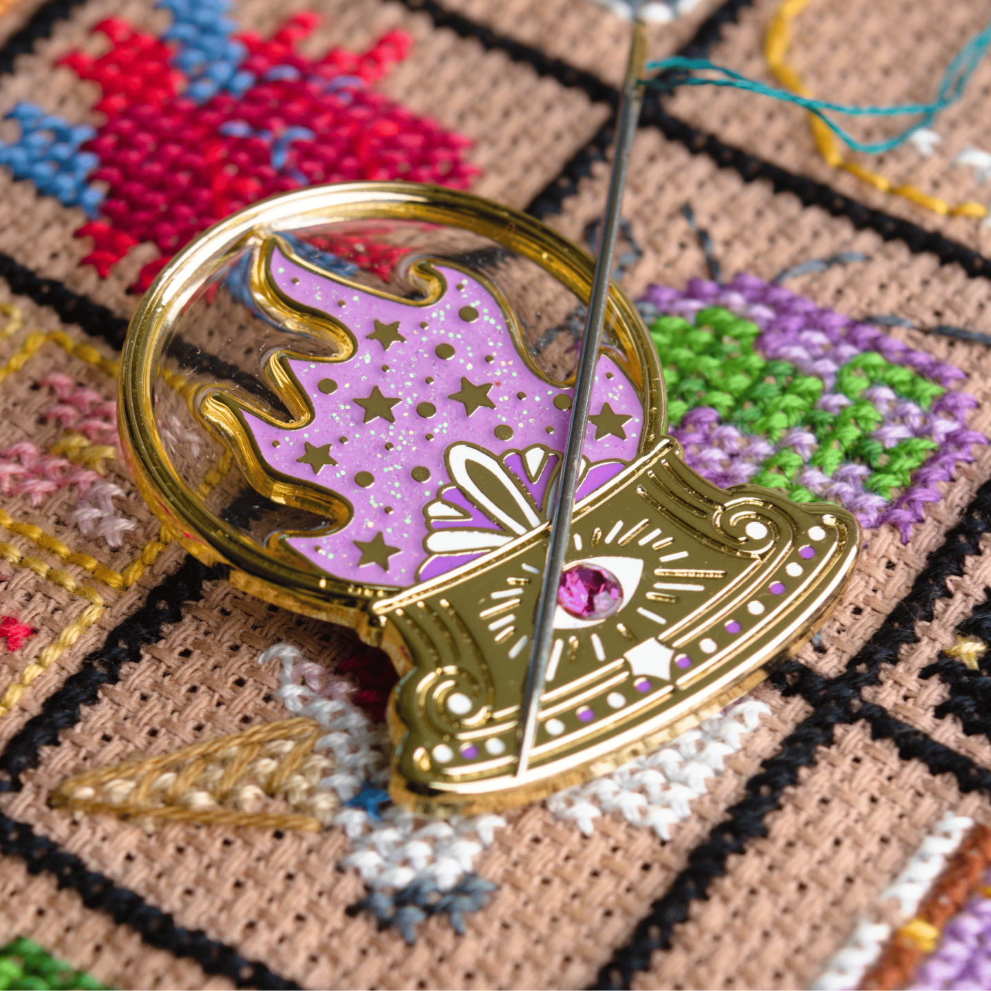 Decorative brooch with fairytale crystal ball design on a cross-stitched background.