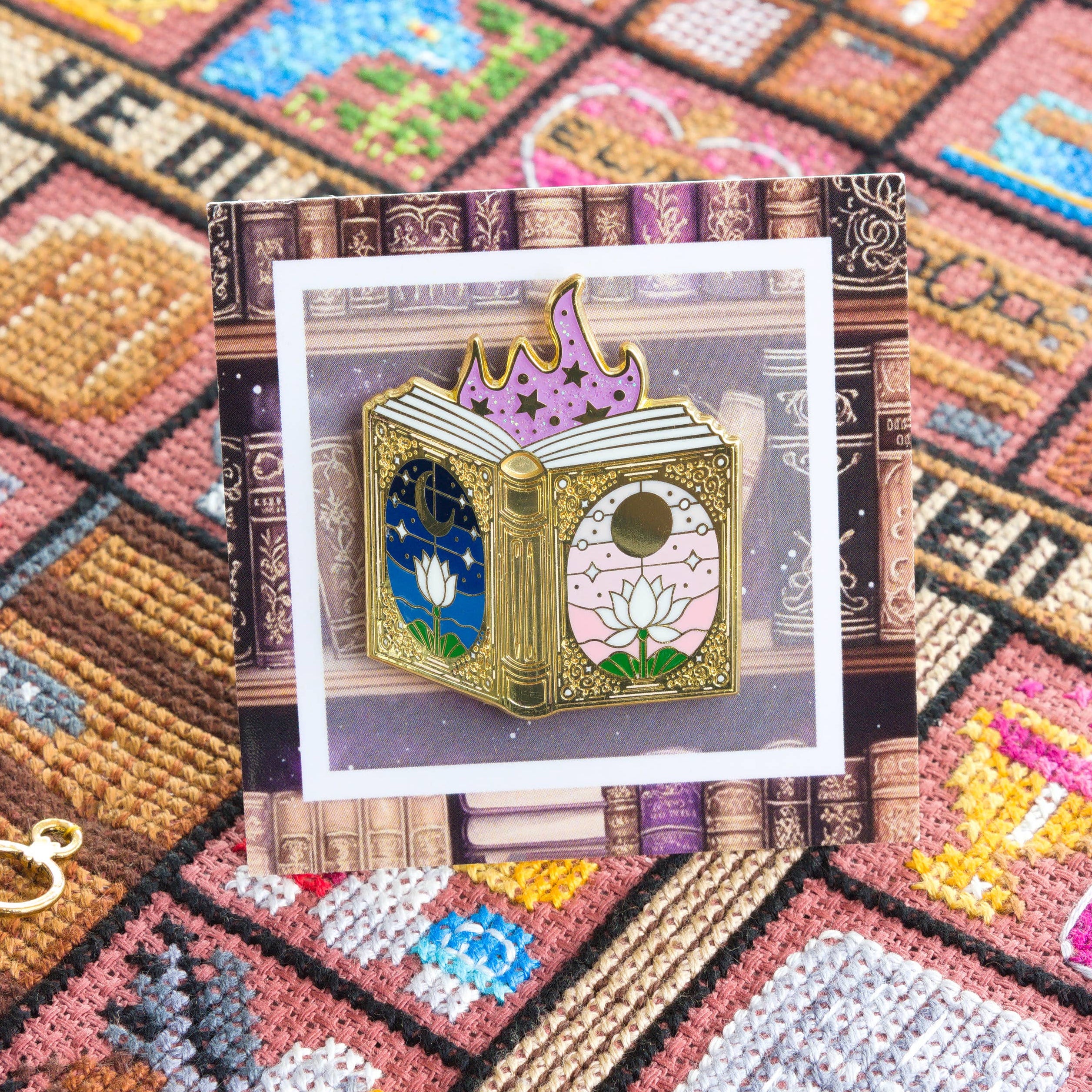 Close-up of a fairy tale book needle minder on a backing card with a book design. The card and needle minder are displayed against cross-stitched pattern background.