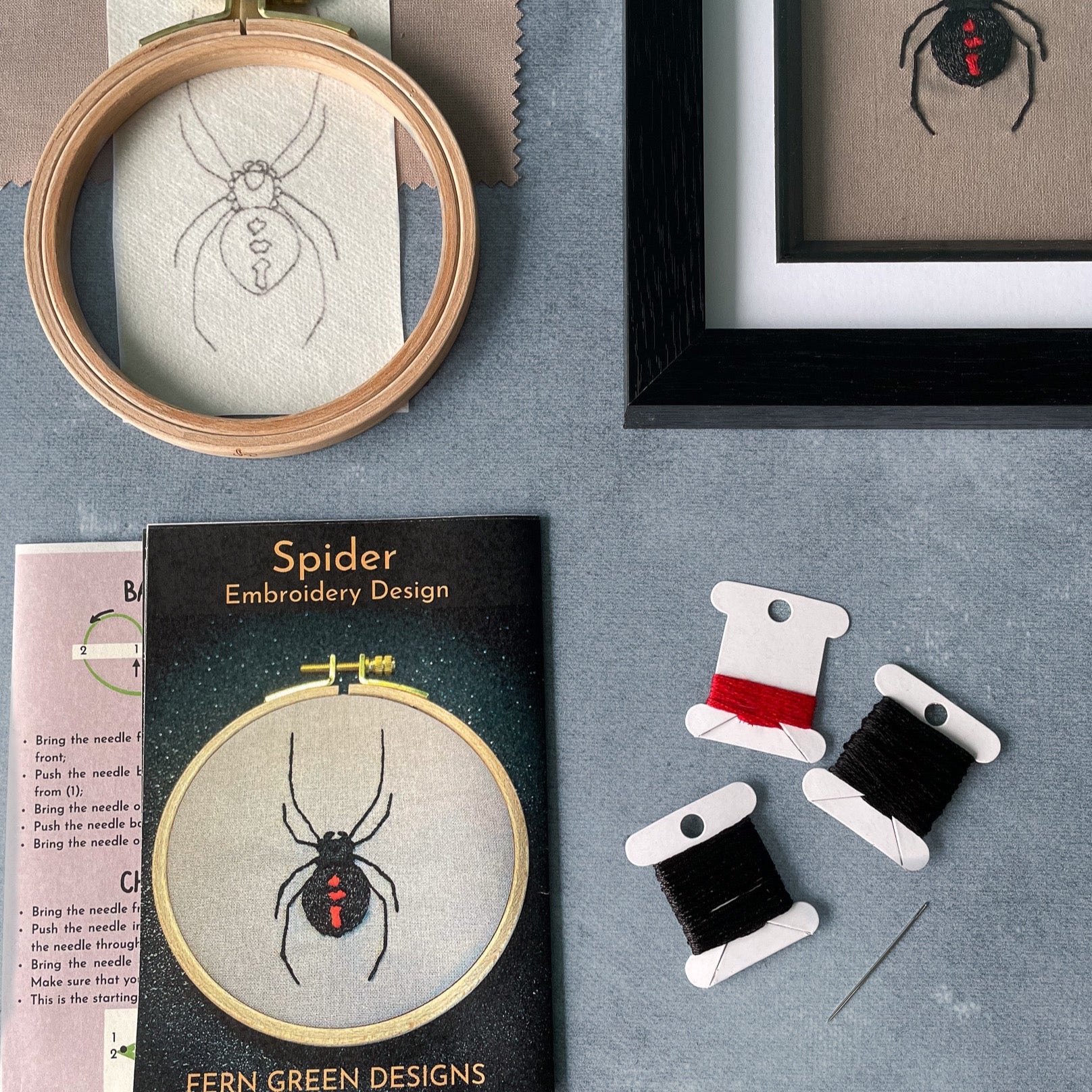 A flat lay image of embroidery kit contents for a spider design. The image shows the completed spider design in one corner and the kit contents spaced neatly to the left and bottom of the finished design. The contents shown are instruction sheet, stitch guide, needle, thread, a hoop, fabric and a pre-drawn spider design.