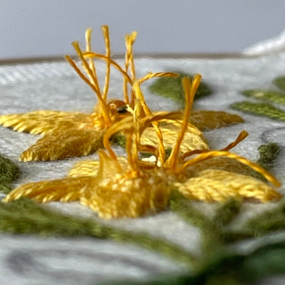 Close-up of embroidered gold and green leaves on fabric with a blurred background