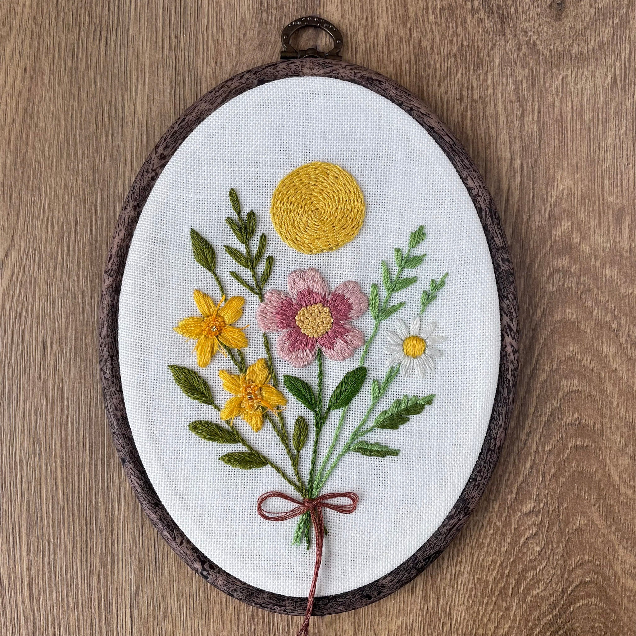 Embroidered floral design in a wooden hoop on a wooden surface