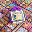 Needle minder shaped like a fairytale book, attached to a backing card with a design showing old books, resting on a purple organza bag.