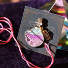 Enamel needle minder of a potion bottle on a decorative card with a colourful background