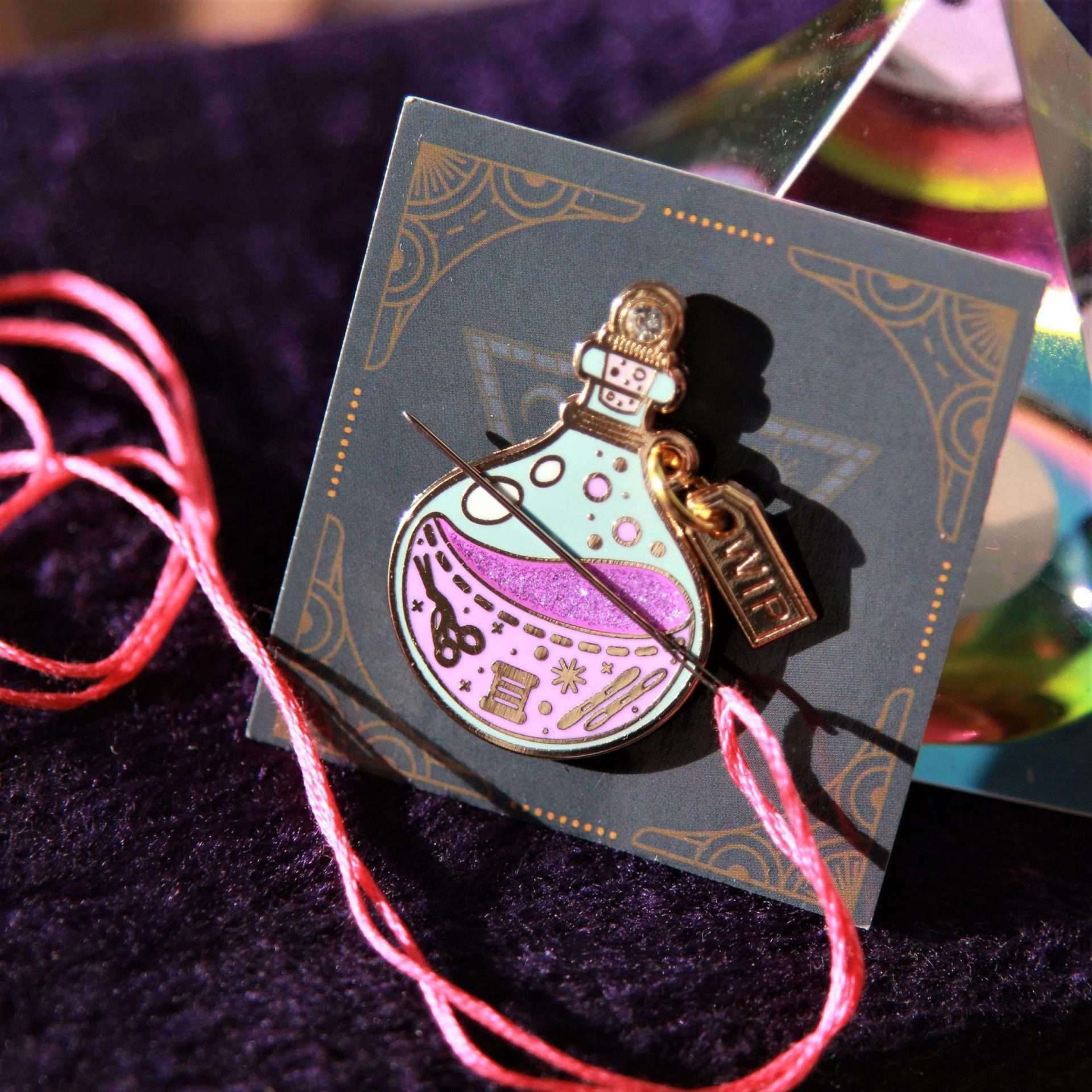 Enamel needle minder of a potion bottle on a decorative card with a colourful background