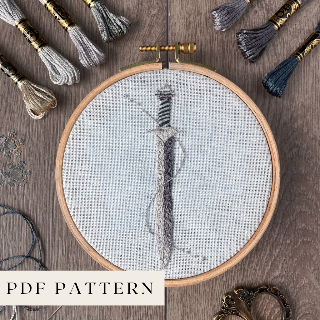 Embroidery hoop with a sword design, surrounded by various embroidery threads and a label indicating 'PDF Pattern'.